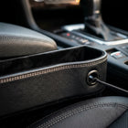 Close-up macro detail of car seat gap organizer highlighting reinforced double stitching and integrated charging cable pass-through port